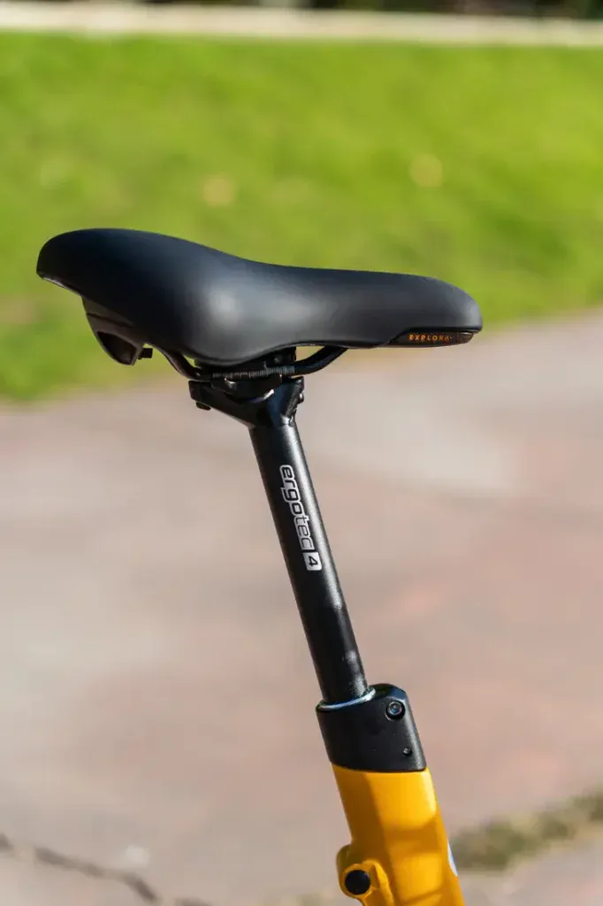 Primer plano de un asiento de bicicleta negro Velo de Ville en una bicicleta amarilla con un fondo de césped verde.