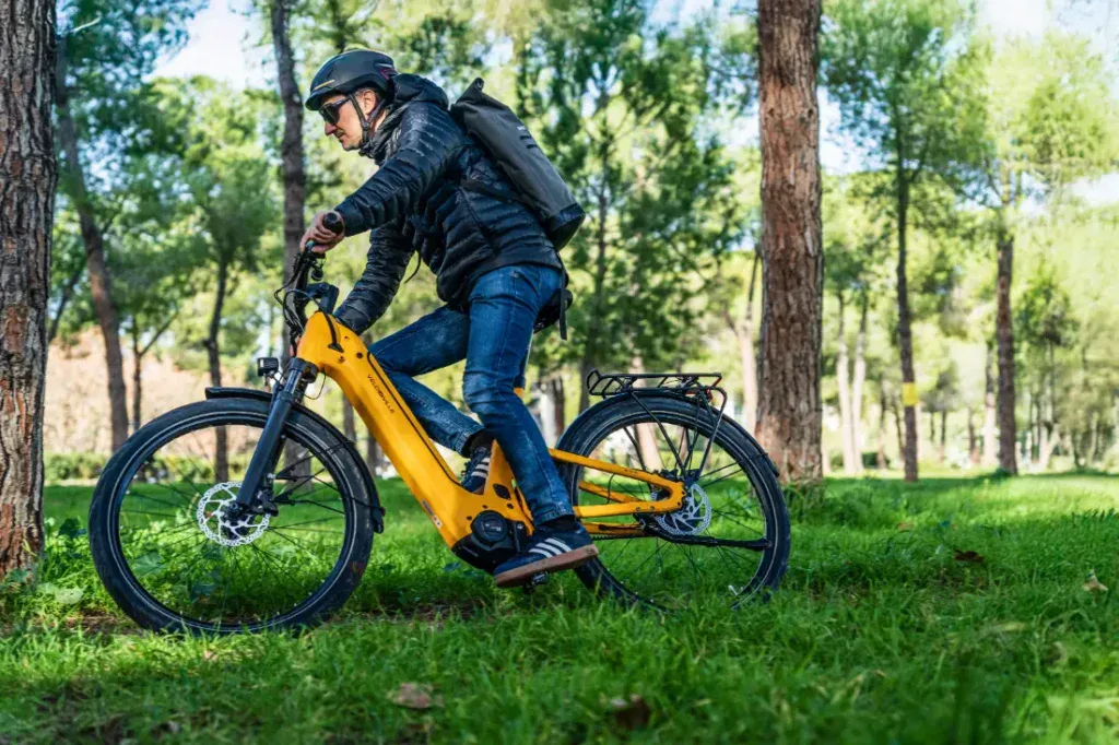 Una persona pasea en una bicicleta eléctrica amarilla Velo de Ville FEB 990 por una zona boscosa, acertando con la opción perfecta para una aventura ecológica.
