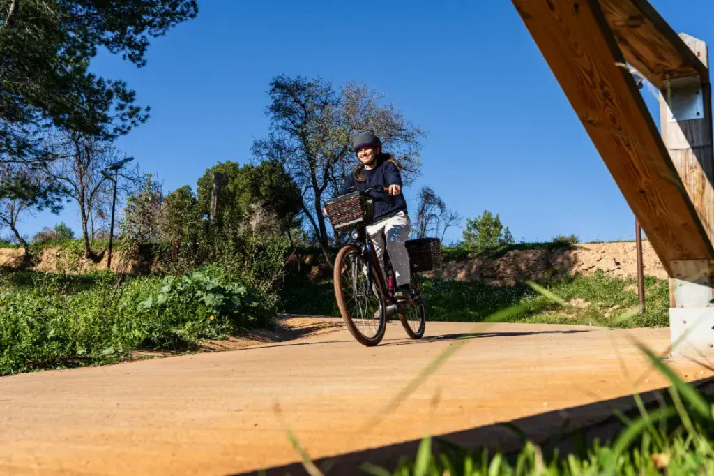Una persona pasea en una Riese & Müller Swing4 Silent por un camino soleado, rodeada de árboles y césped, abrazando el estilo holandés de esta bici eléctrica urbana.