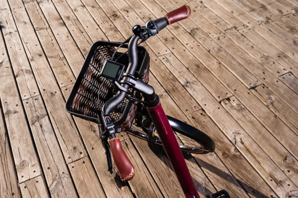 Una encantadora bicicleta roja con manillar de cuero marrón y una cesta de mimbre adorna el paseo marítimo de madera, mostrando su diseño de estilo holandés.