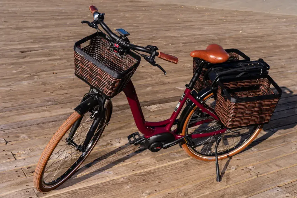 Una bicicleta eléctrica de color marrón con cestas de madera se encuentra elegantemente sobre una plataforma de madera, capturando una encantadora vibra de estilo holandés.