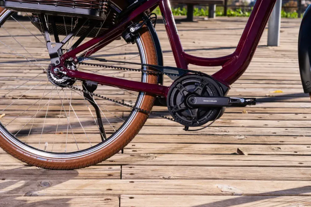 Primer plano de la rueda trasera y el pedal de una bicicleta marrón sobre una plataforma de madera, capturando su estilo urbano elegante que recuerda a los diseños clásicos de estilo holandés.