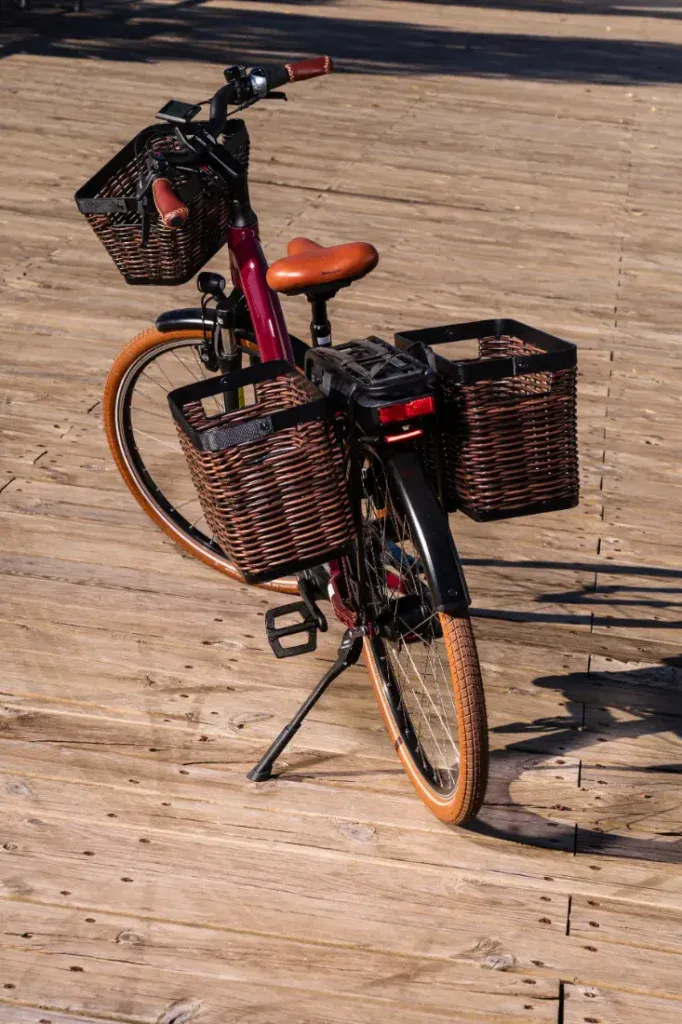 Una bicicleta, con cestas de mimbre marrón en el clásico estilo holandés, descansa sobre una pasarela de madera bajo la luz del sol.