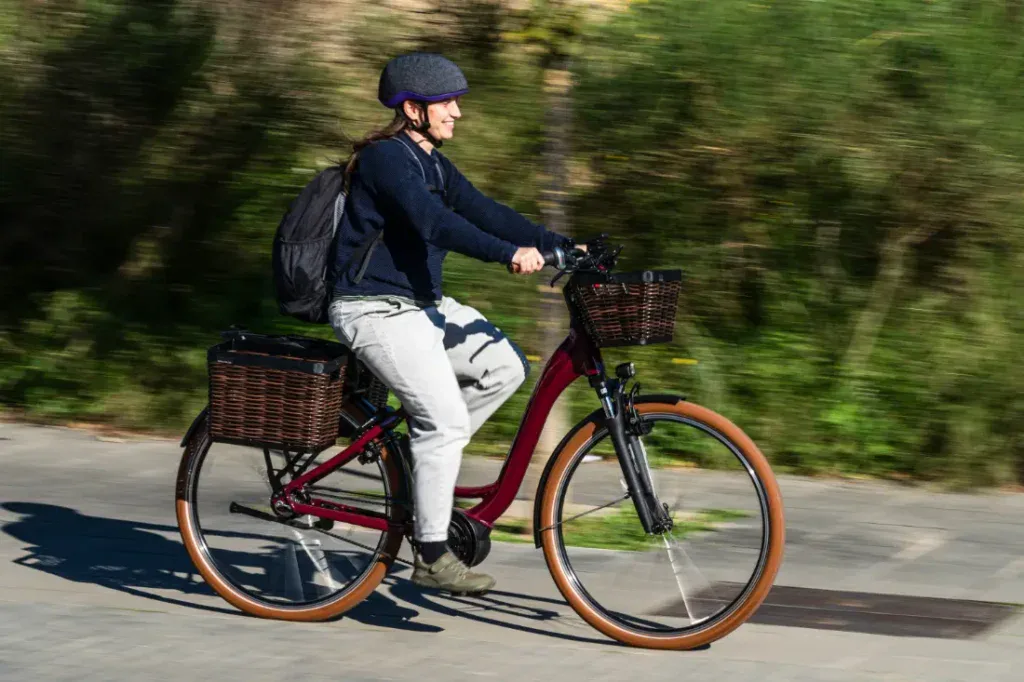 Una persona conduce una Riese & Müller Swing4 Silent roja, con casco y mochila, por un camino soleado con vegetación de fondo.