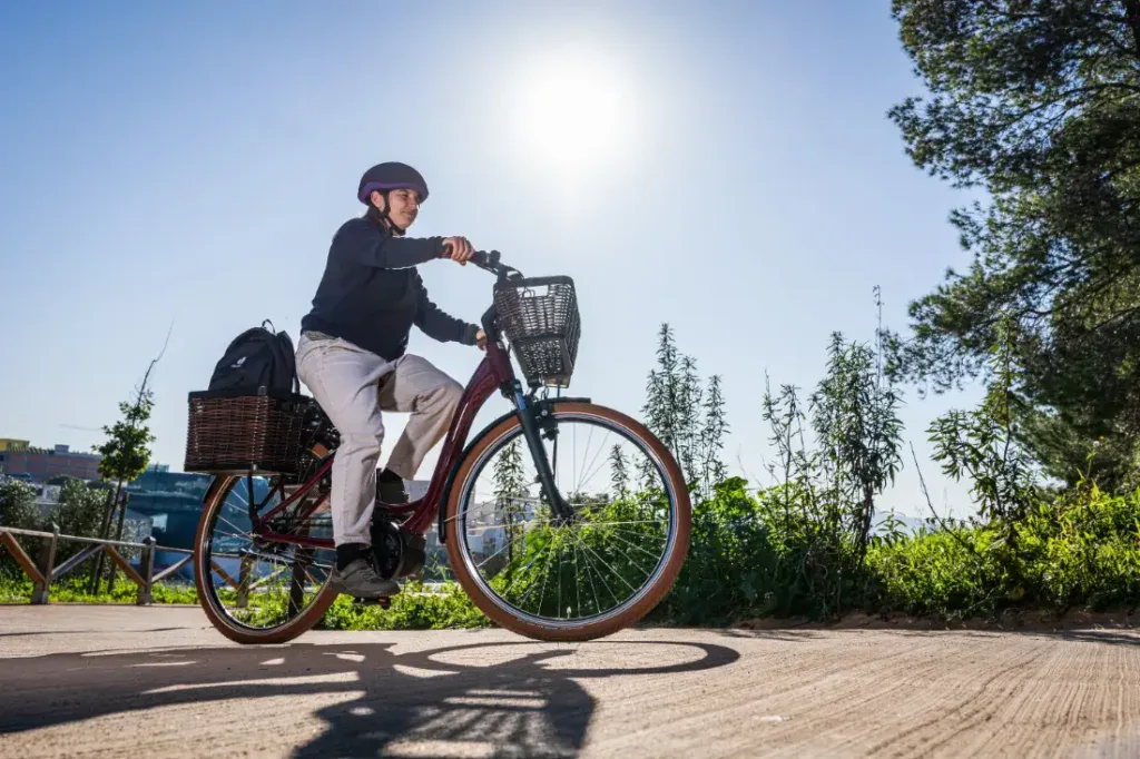 Ciclismo en un día soleado, con casco puesto y llevando una mochila en una cesta, la persona pedalea sin esfuerzo su bicicleta eléctrica urbana Riese & Müller a través de una exuberante vegetación.