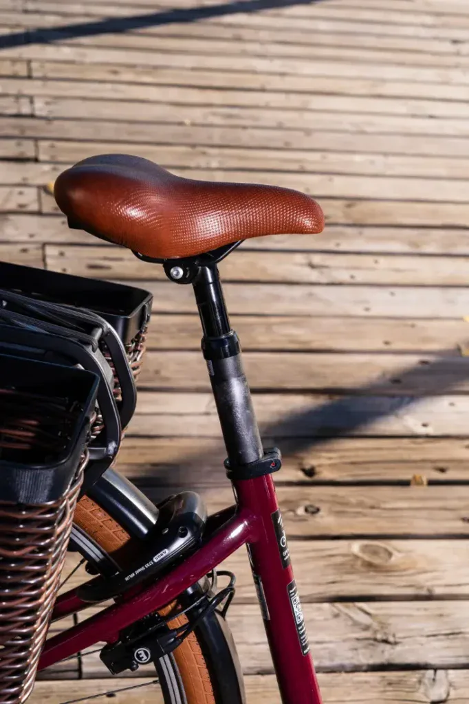 Primer plano de un asiento de bicicleta y una cesta Riese & Müller Swing4 Silent sobre una pasarela de madera a la luz del sol, mostrando la elegancia del diseño de estilo holandés.