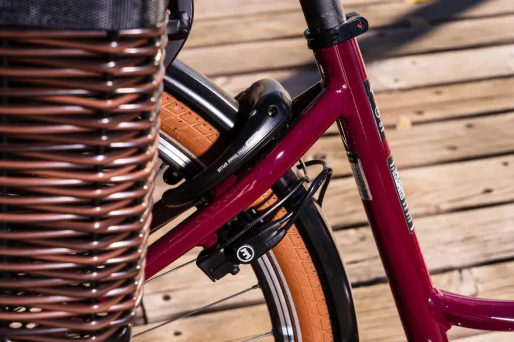 Primer plano de un cuadro de bicicleta Riese & Müller marrón con una canasta de mimbre y neumáticos de color tostado anaranjado, que irradia un encanto de estilo holandés sobre una plataforma de madera.